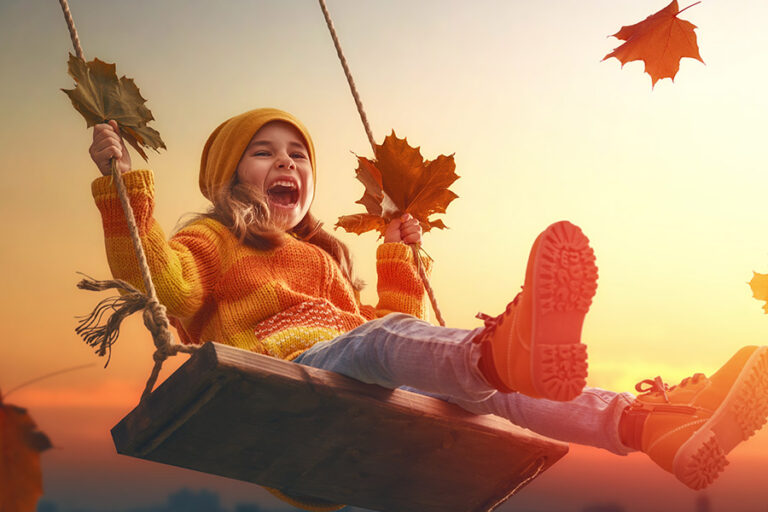 Herfst plezier - meisje op een schommel met herfstbladeren in haar hand